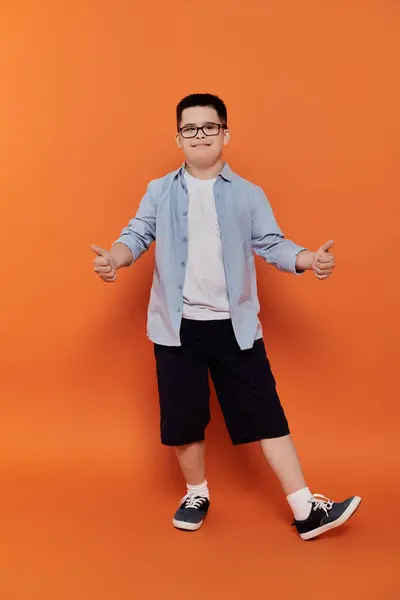 Young boy with Down syndrome smiles, arms outstretched in front of orange backdrop. — Stock Photo
