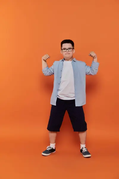 A young boy with Down syndrome flexes his muscles in front of an orange background. — Stock Photo