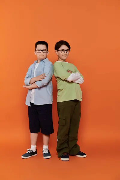 Dois meninos, um com síndrome de Down, ficar com os braços cruzados na frente de um fundo laranja. — Fotografia de Stock