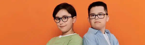 Two young boys, one with Down syndrome, pose together in front of an orange background. — Stock Photo