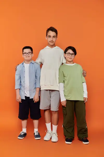 Three young boys stand together in front of an orange background. — Stock Photo