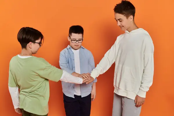 Trois jeunes garçons, l'un avec le syndrome de Down, se tiennent ensemble dans un home studio avec les mains empilées dans l'unité. — Photo de stock