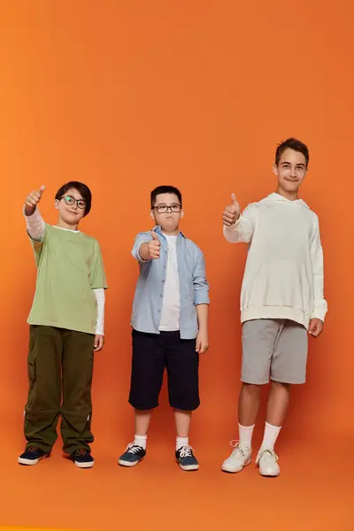 Three boys, including one with Down syndrome, pose for a portrait with thumbs up. — Stock Photo