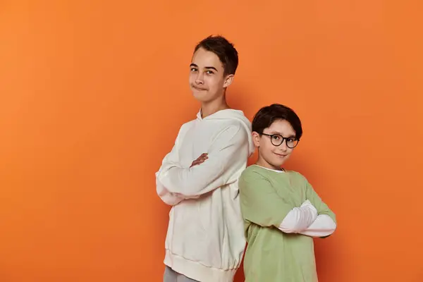 Two young boys stand side by side in front of a bright orange wall, smiling at the camera. — Stock Photo