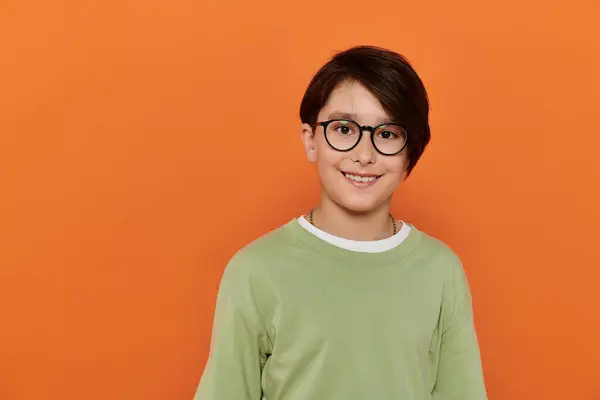 A young boy with glasses smiles brightly against an orange backdrop. — Stock Photo