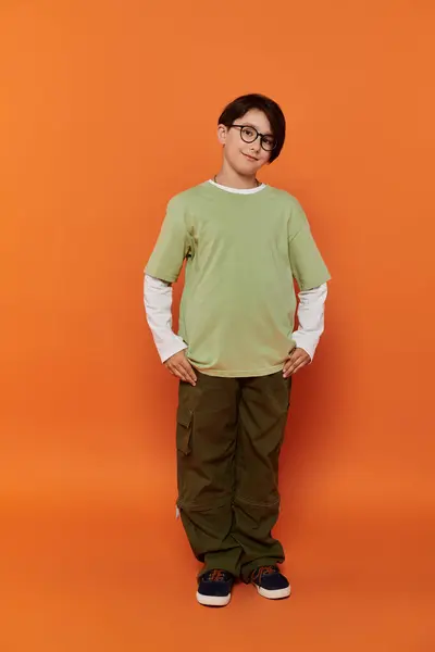 A young boy stands confidently with hands on hips, wearing a green shirt and khaki pants. — Stock Photo