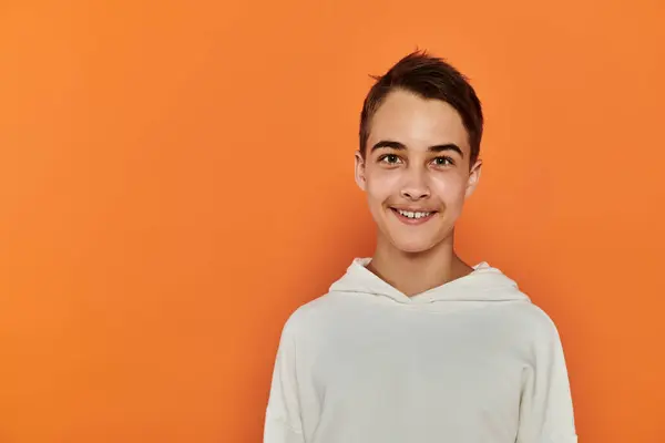 A young boy smiles brightly against a solid orange backdrop. — Stock Photo