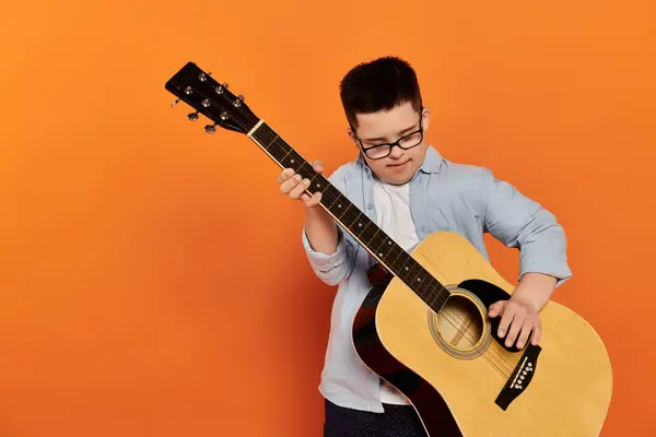 A young boy plays the guitar in front of an orange background. — Stock Photo