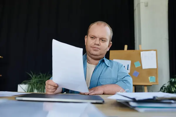 A man with inclusivity sits at a desk, reviewing paperwork. — Stock Photo
