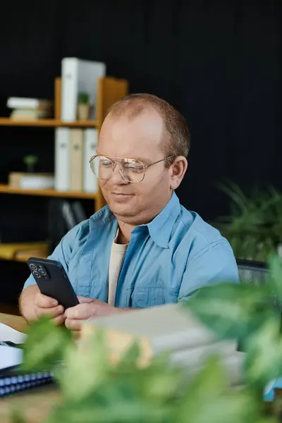 A man with inclusivity wearing glasses sits at a desk, concentrated on his mobile phone. — Stock Photo