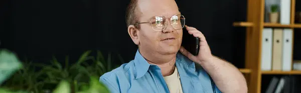 A man with inclusivity in glasses talks on the phone in his office, surrounded by plants and a bookshelf. — Stock Photo