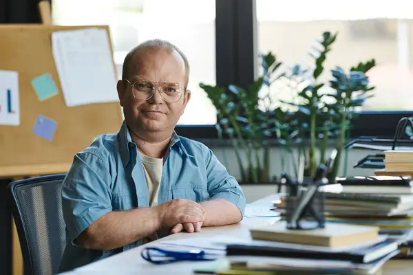 A man with inclusivity wearing glasses sits at a desk in an office. — Stock Photo