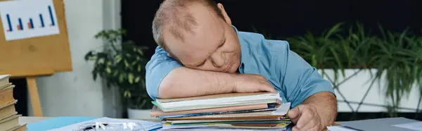 A man with inclusivity in a blue shirt is sleeping on a large stack of papers in an office setting. — Stock Photo