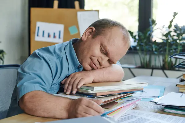 A man with inclusivity takes a nap at his desk, resting his head on a stack of papers. — Stock Photo