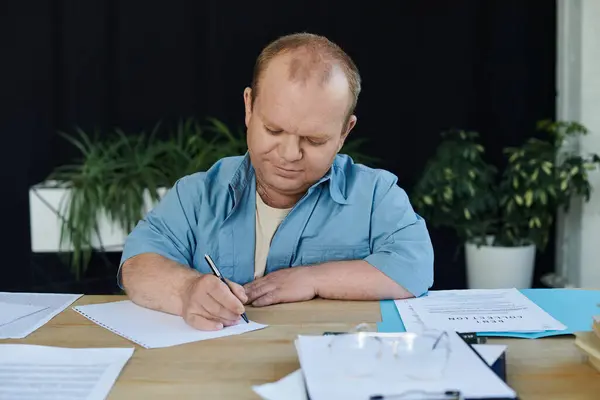 A man with inclusivity sits at a desk, intently writing on a sheet of paper. — Stock Photo