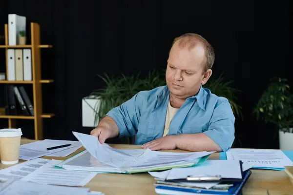 A man with inclusivity sits at a desk, diligently reviewing paperwork. — Stock Photo