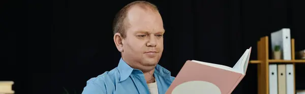 Ein Mann mit Inklusivität sitzt nachdenklich in einem Buch, sein Blick starr auf die offenen Seiten gerichtet.. — Stockfoto
