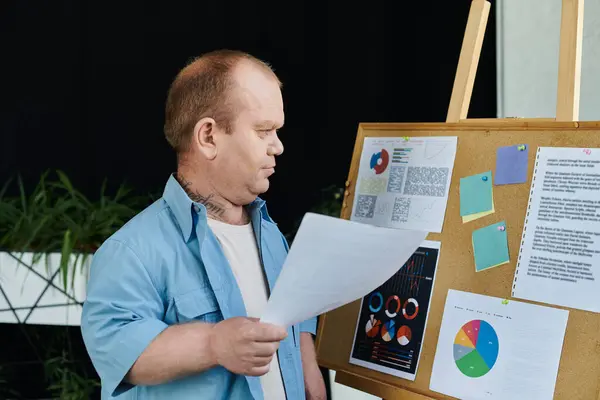 A man with inclusivity stands before a corkboard, reviewing charts and data. — Stock Photo
