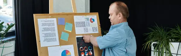 A man with inclusivity is standing next to a corkboard, presenting charts and graphs. — Stock Photo