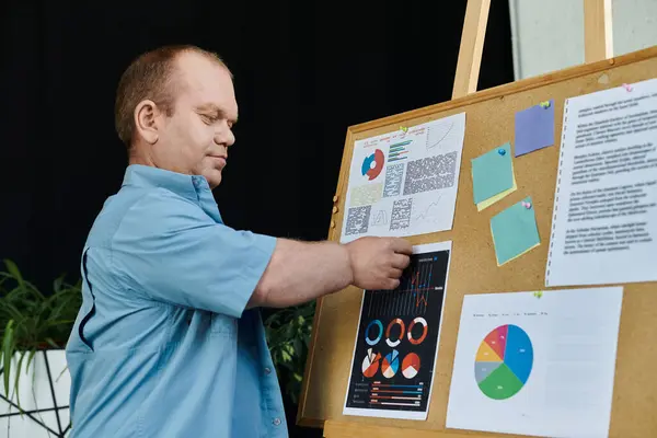 A man with inclusivity in a blue shirt stands in front of a corkboard, examining graphs and charts. — Stock Photo