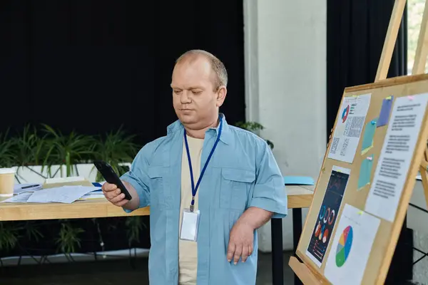 A man with inclusivity stands in an office, intently looking at his smartphone. — Stock Photo