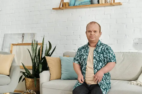 A man with inclusivity in a floral shirt sits on a grey sofa in a modern living room. — Stock Photo
