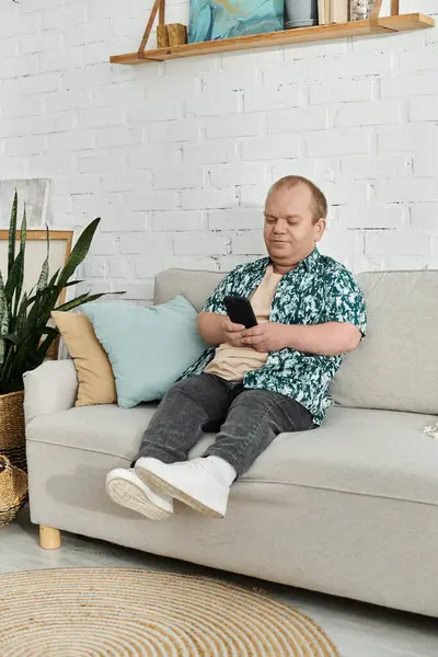 A man with inclusivity is sitting on a sofa, comfortably using his phone. — Stock Photo