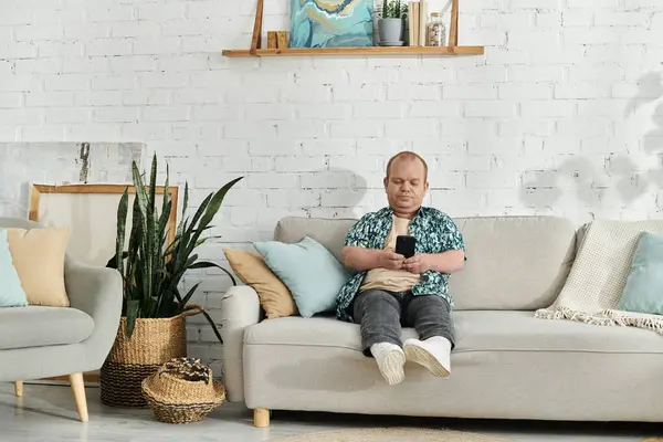 A man with inclusivity sits on a couch in a living room, casually looking at his phone. — Stock Photo