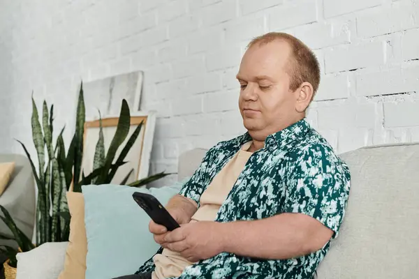 A man with inclusivity sits on a couch, looking at his phone. — Stock Photo
