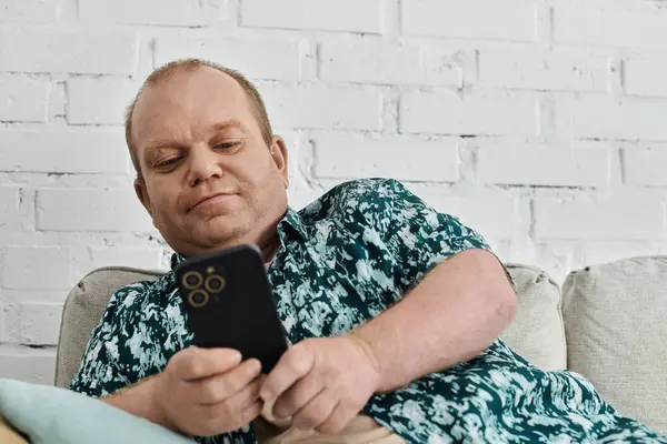 A man with inclusivity is sitting on a sofa, looking at his phone. — Stock Photo
