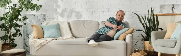 A man with inclusivity is sitting on a white couch in a living room with plants. — Stock Photo