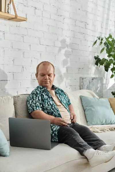 A man with inclusivity sits on a couch with a laptop in his lap, looking relaxed and at ease. — Stock Photo