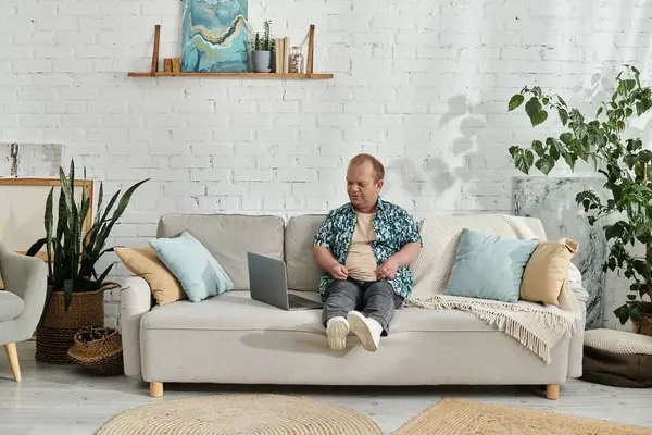 Um homem com inclusividade está sentado em um sofá em uma sala de estar, usando um laptop. — Fotografia de Stock