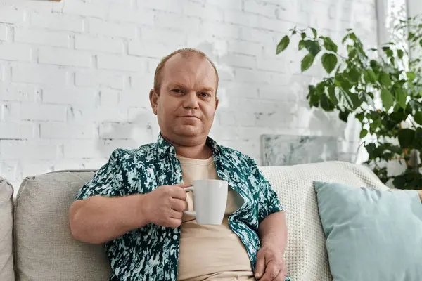 A man with inclusivity sits on a couch, holding a cup, in a home setting. — Stock Photo