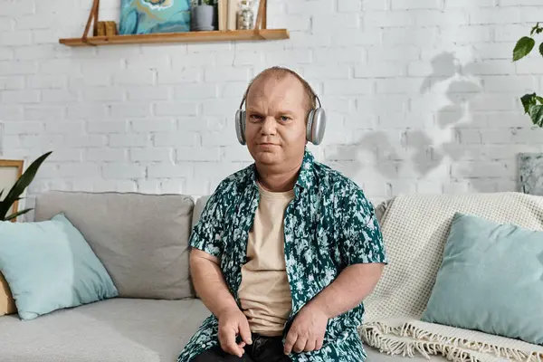 Mann mit Inklusivität sitzt mit Kopfhörer und gemustertem Hemd auf Couch und genießt gemütlich Musik. — Stockfoto
