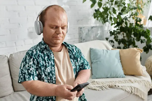 A man with inclusivity wearing headphones sits on a couch, looking down at his phone. — Stock Photo