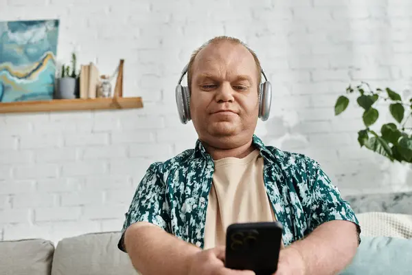 A man with inclusivity wearing headphones listens to music while scrolling through his phone. — Stock Photo