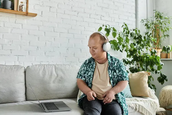 Ein Mann mit Kopfhörern sitzt auf einer Couch und benutzt einen Laptop. — Stockfoto