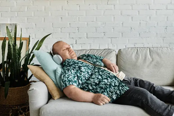 A man with inclusivity relaxes on a gray couch with a white brick wall backdrop. — Stock Photo