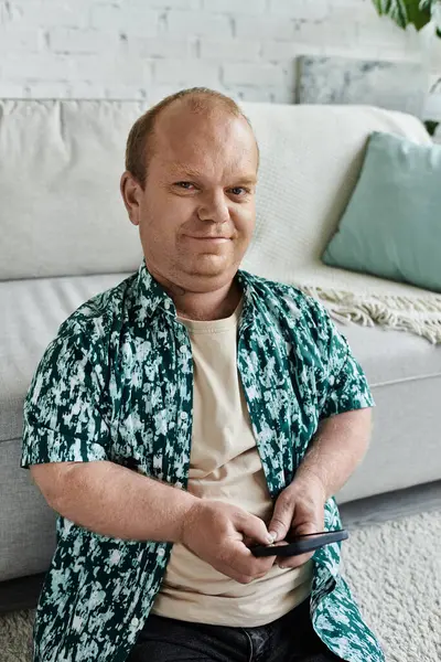 A man with inclusivity sits on the floor, relaxed and engaged with his phone. — Stock Photo
