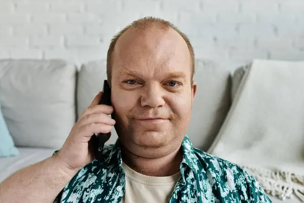 A man with inclusivity sits on a couch, engaged in a phone conversation. — Stock Photo