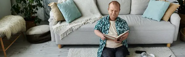 Un hombre con inclusividad se sienta en un sofá, absorto en un libro, disfrutando de un tranquilo momento de relajación. — Stock Photo