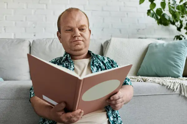 A man with inclusivity sits on a couch, engrossed in a book, in a living room setting. — Stock Photo