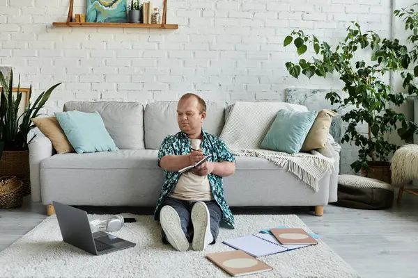 Um homem com inclusividade senta-se no chão de uma sala de estar, focado em escrever em um caderno. — Fotografia de Stock