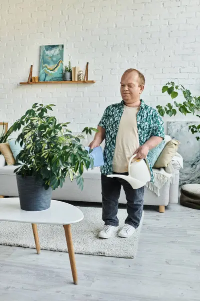 A man with inclusivity waters a potted plant in a bright, modern living room. — Stock Photo