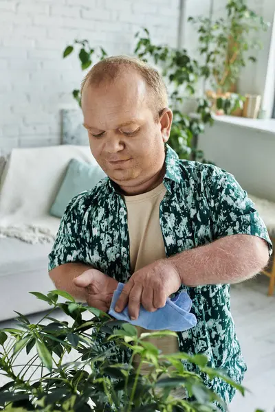 Человек с инклюзивностью тщательно вытирает листья растения в горшке синей тканью. — стоковое фото
