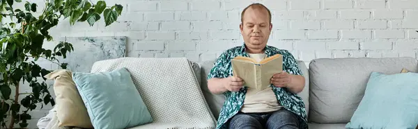 A man with inclusivity sits on a couch reading a book. — Stock Photo