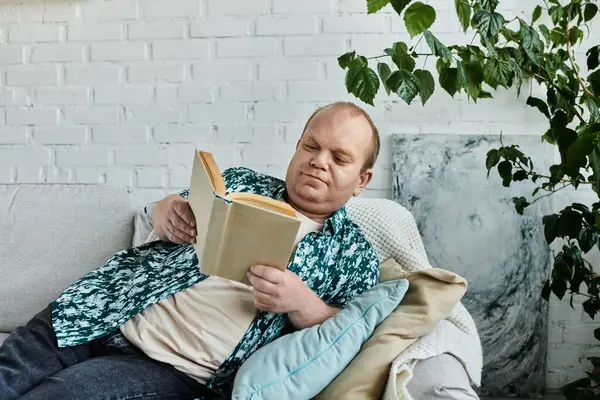 A man with inclusivity relaxes on a couch, absorbed in the pages of a book. — Stock Photo