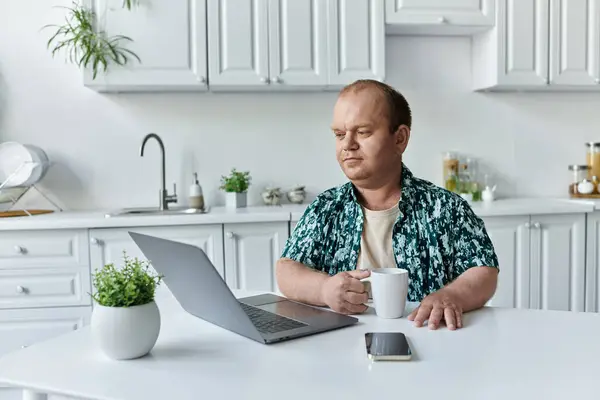 Ein inklusiver Mann sitzt an einem Küchentisch und arbeitet an einem Laptop. — Stockfoto