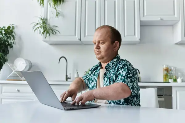 Um homem com inclusividade trabalha em seu laptop em uma mesa de cozinha branca. — Fotografia de Stock